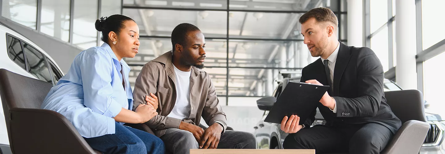 Car salesman showing a couple something on a clipboard in a car dealership