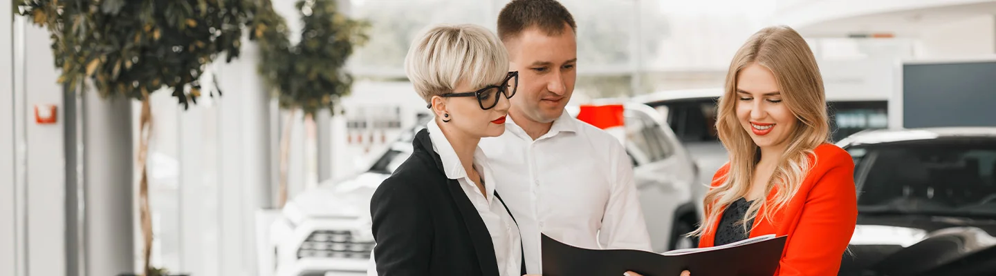 couple looking over car specification with another person in dealership