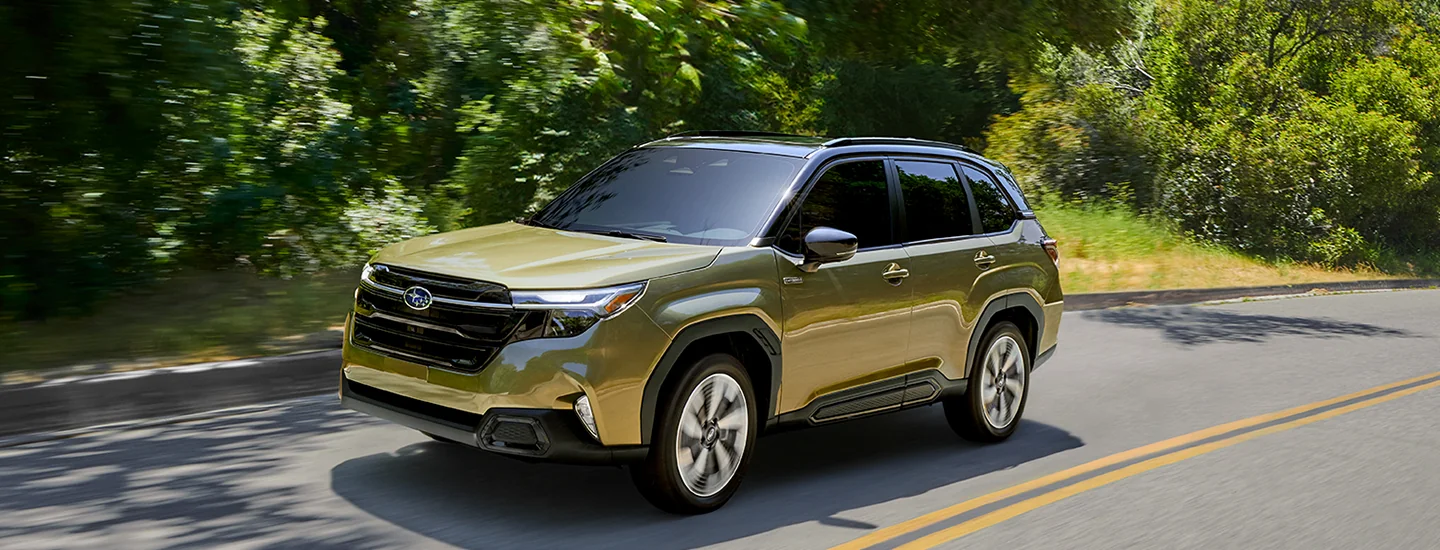 Front side view of a gold 2024 Subaru Forester driving on a back road next to a forest in South Chesterfield, VA.