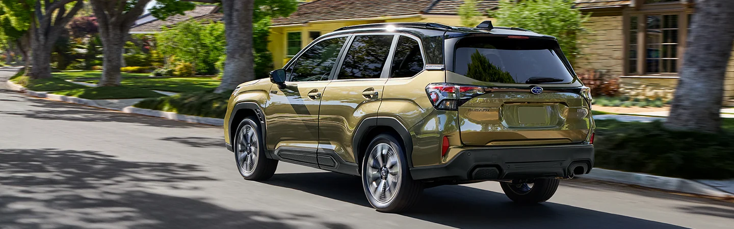 Back side view of a gold 2025 Subaru Forester driving past a house in a neighborhood in South Chesterfield, VA.