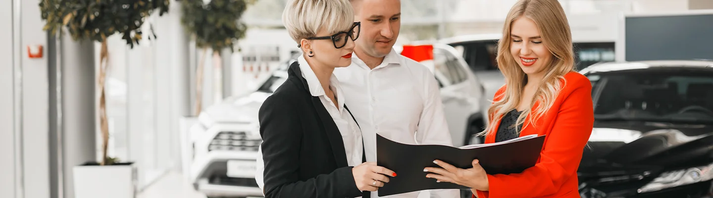two people speaking with car salesperson going over details of car purchase in the dealership showroom