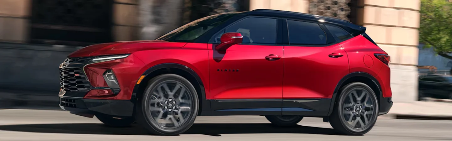 Side view of a red 2025 Chevrolet Blazer 2LT driving in the city