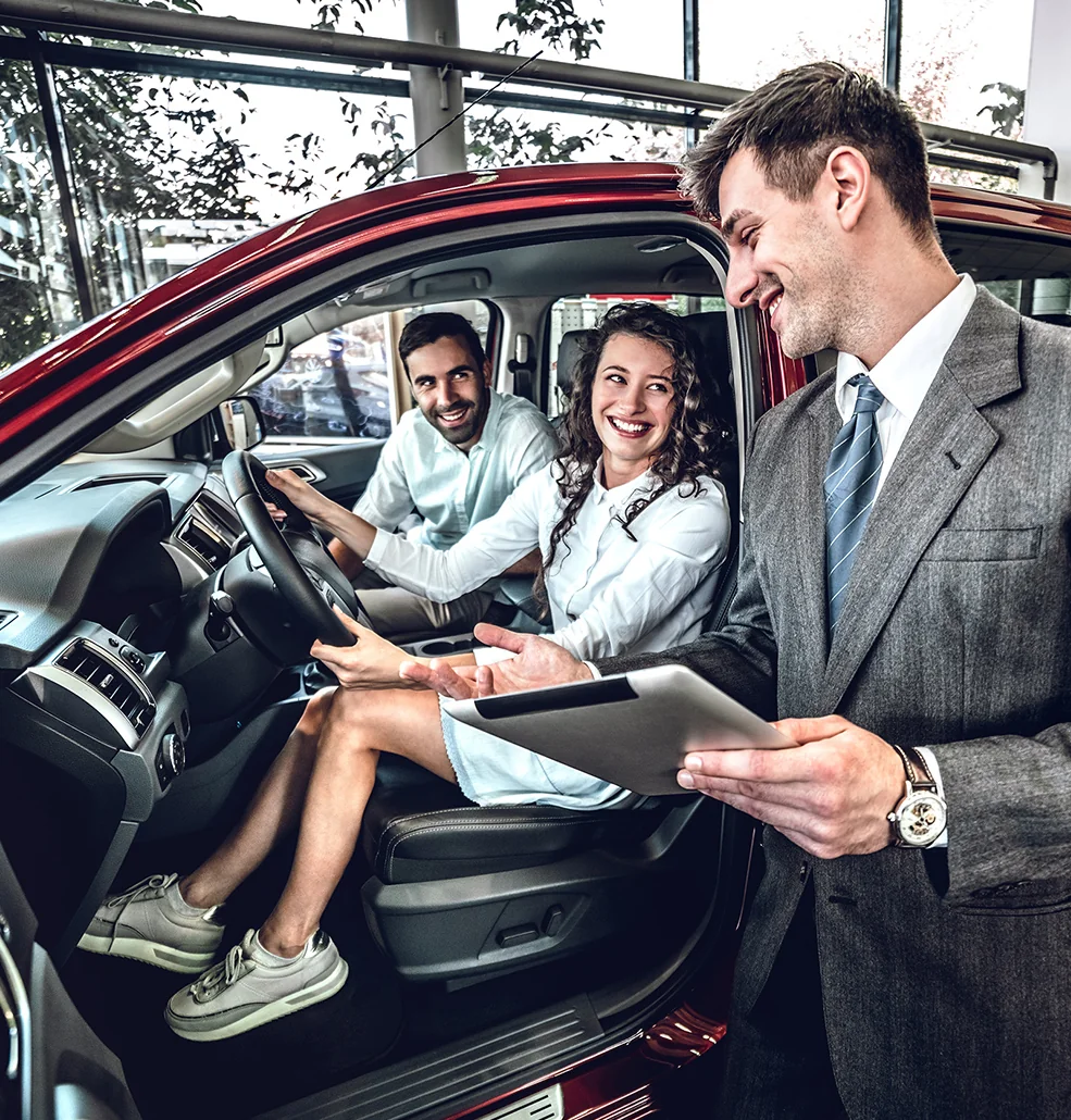 A man and woman sitting together in a car, both smiling and looking ahead.