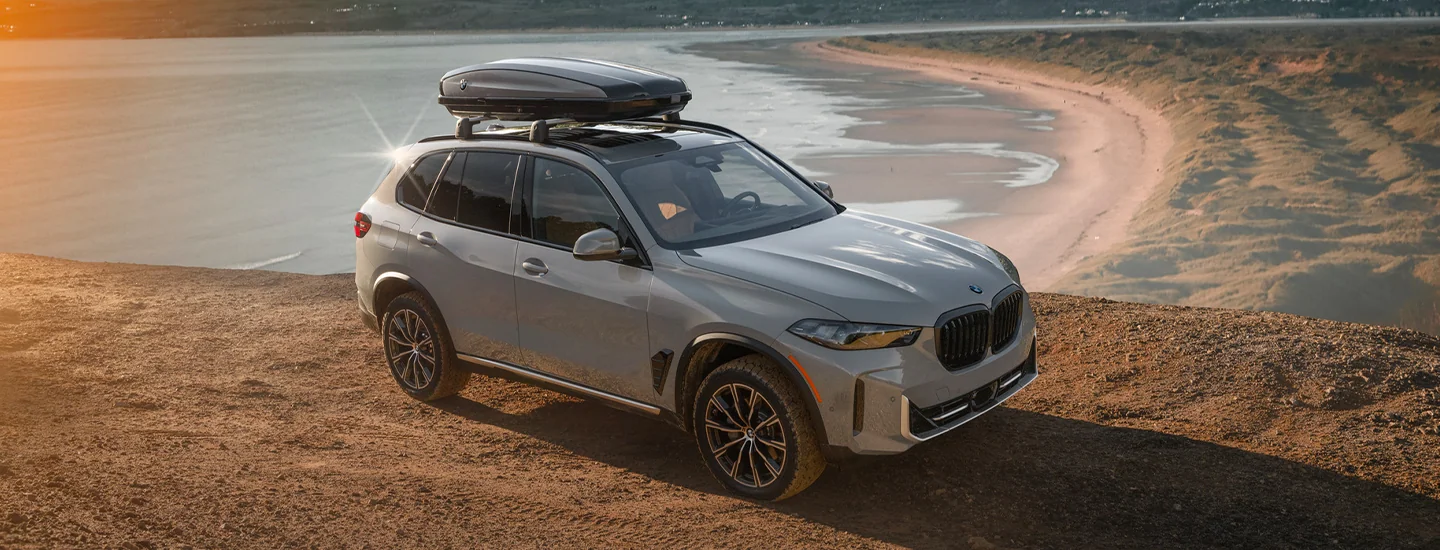 a 2025 BMW X5 parked at scenic overlook to a beach with a roof luggage compartment on top