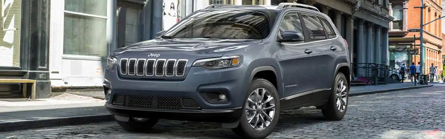 A grey Jeep Cherokee parked along the street in the city.