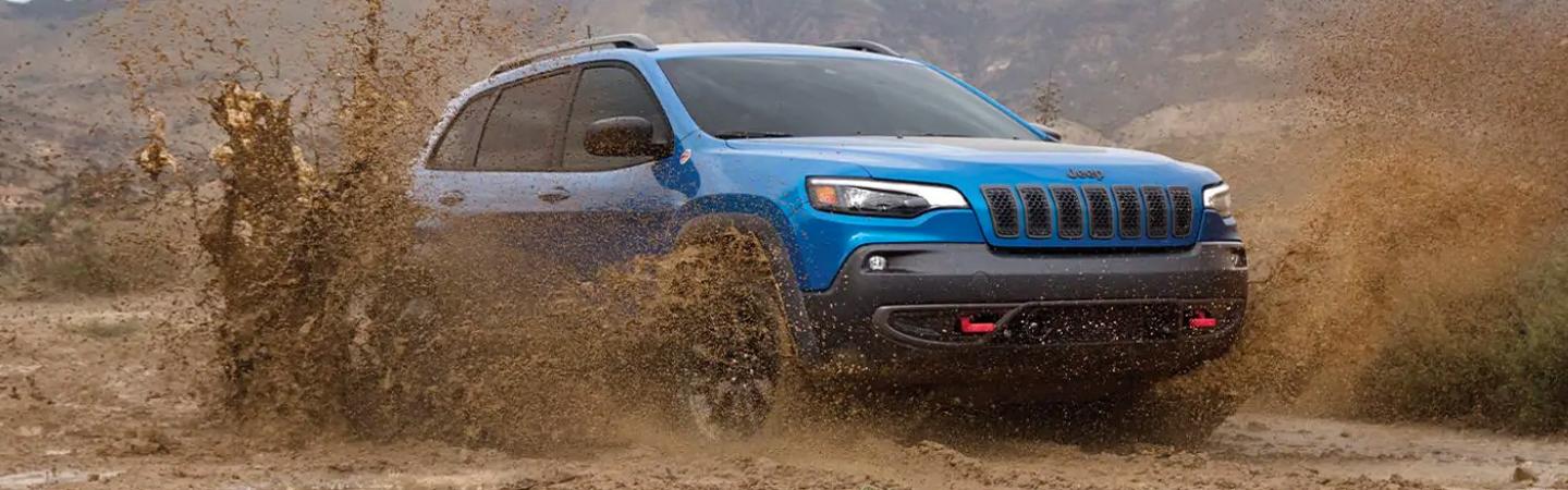A blue Jeep Cherokee kicking up mud.