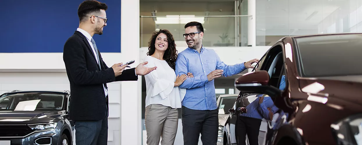 A couple looking at a new car with a car salesman talking to them