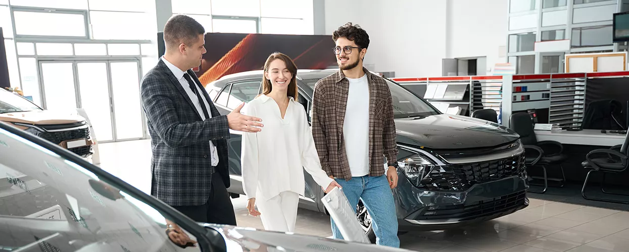 What Are the Best 2026 Hyundai Sonata Hybrid Lease Deals Near Baltimore, MD? in three people walking through a car dealership with the vehicles around them