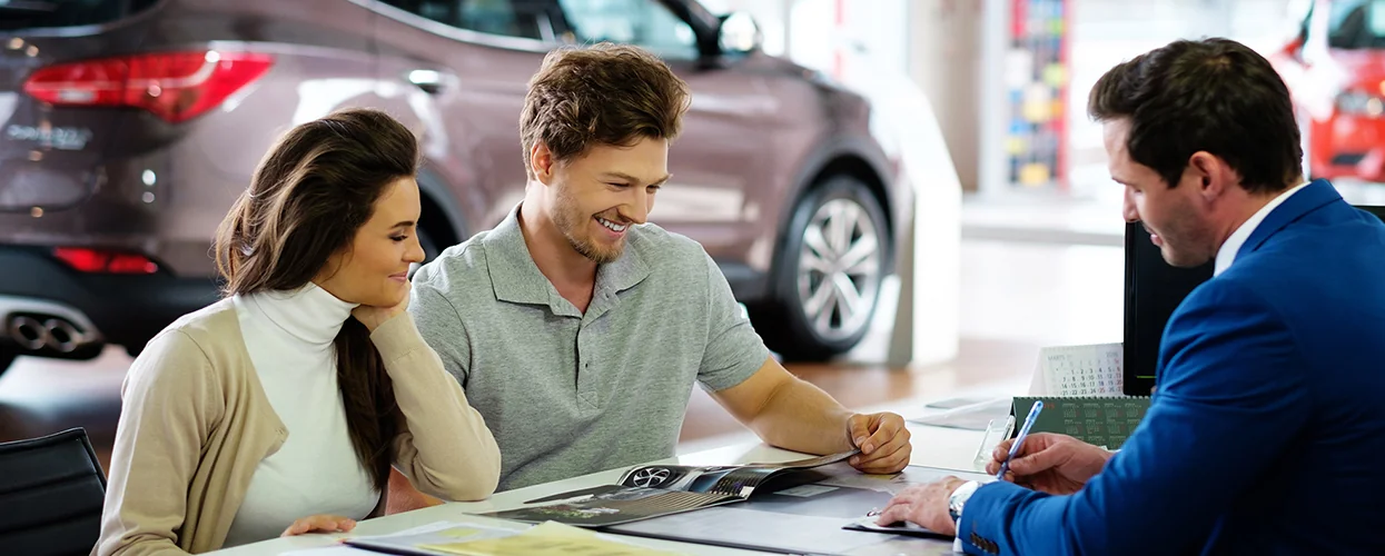 couple speaking with car salesman in showroom