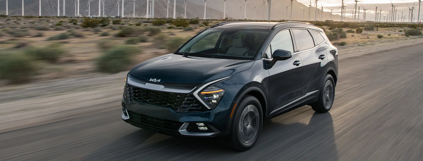 2025 Kia Sportage Hybrid driving on a road next to a wind farm