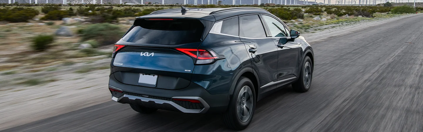 Back view of a 2025 Kia Sportage Hybrid driving on a road next to a wind farm