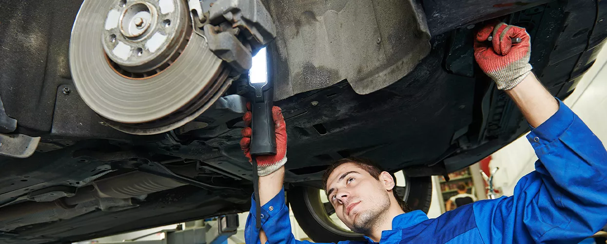 Certified automotive technician inspecting a vehicle undercarriage during maintenance and repair service in a professional auto shop