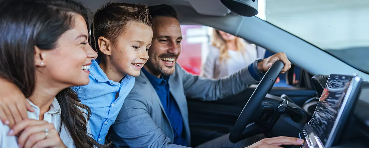 Family exploring a new vehicle's touchscreen infotainment system during a dealership showroom visit