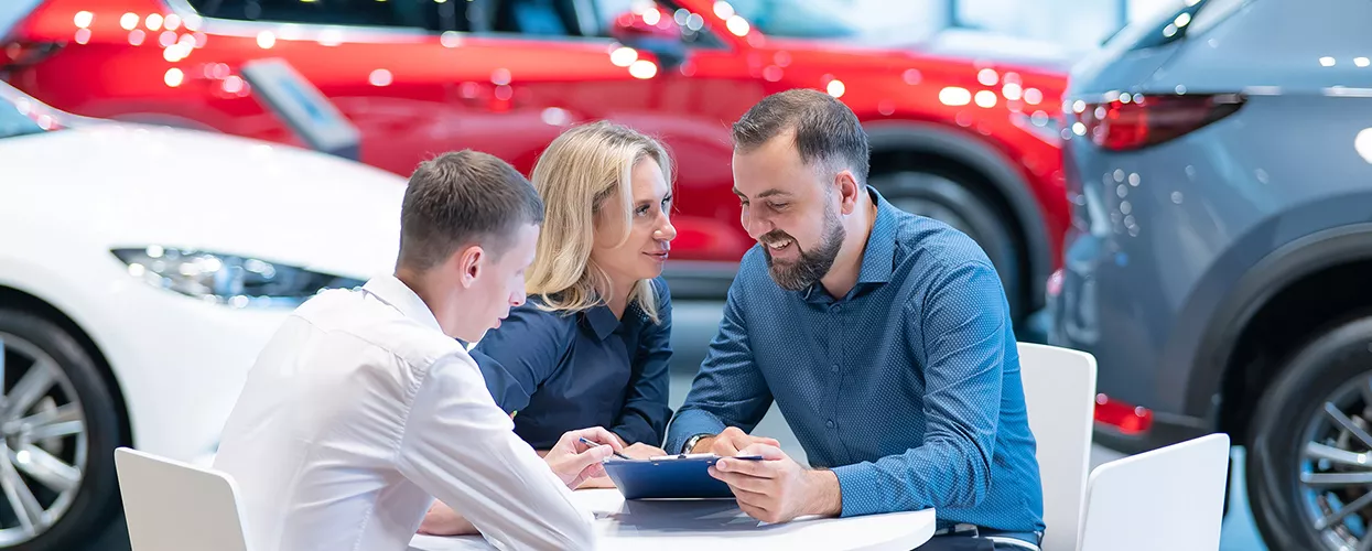 Three people sitting at a table in a car dealership looking at a document