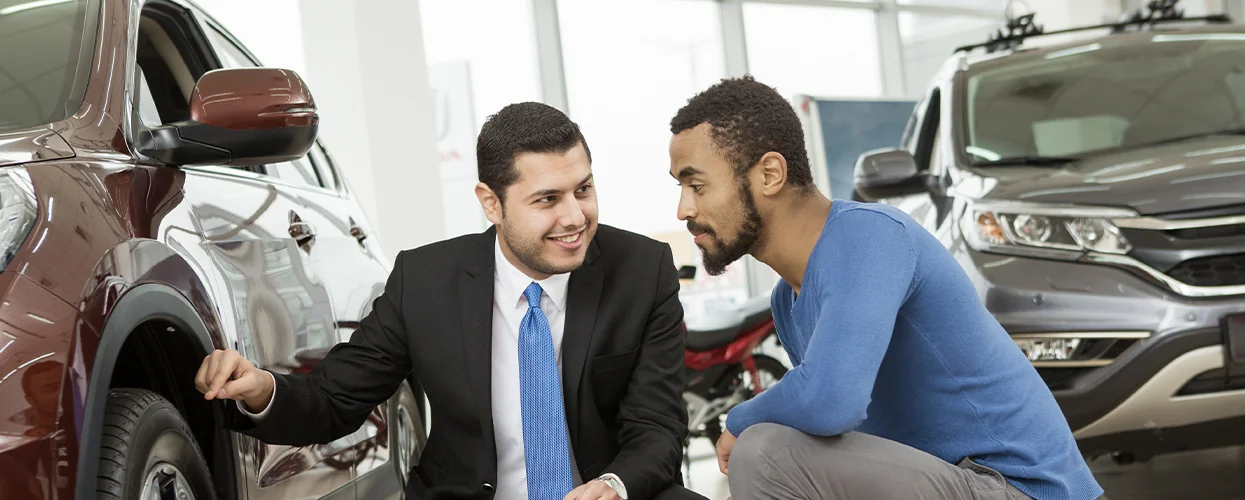 Two men in suits examining a car, discussing its features and specifications.