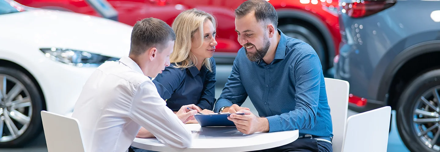 a happy couple seated at a table with salesperson going over new car financing