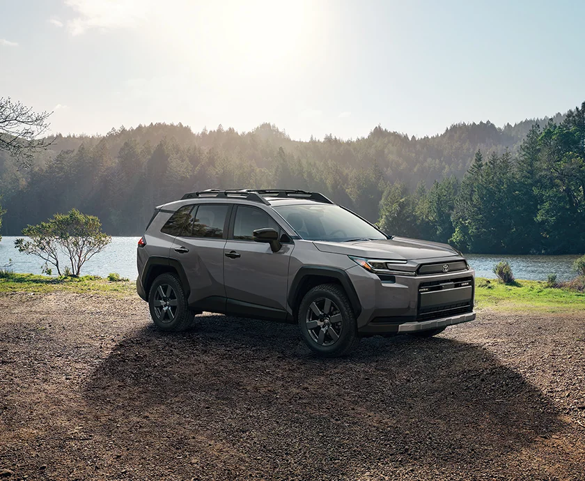 A 2020 Toyota RAV4 parked on a dirt road near a tranquil lake, with lush greenery in the background.