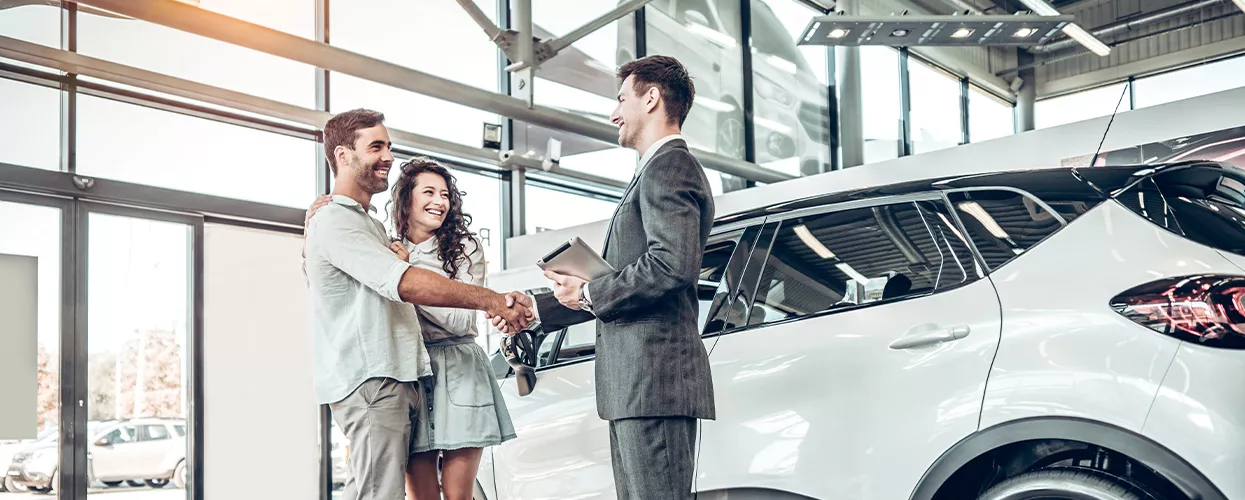 Couple shaking hands with a car salesman in a car dealership