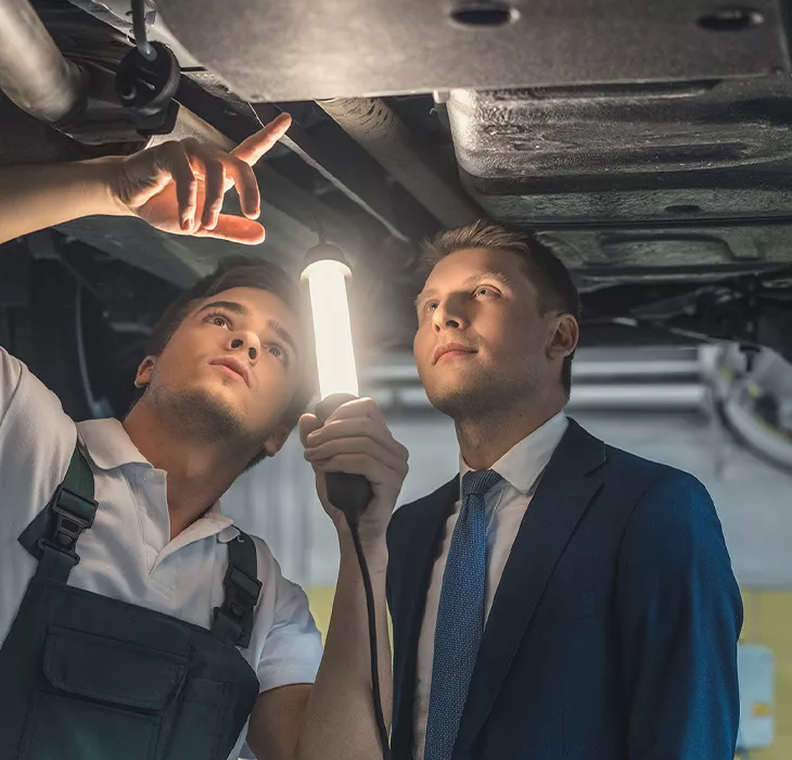 mechanic and service manager looking at repairs under a car.