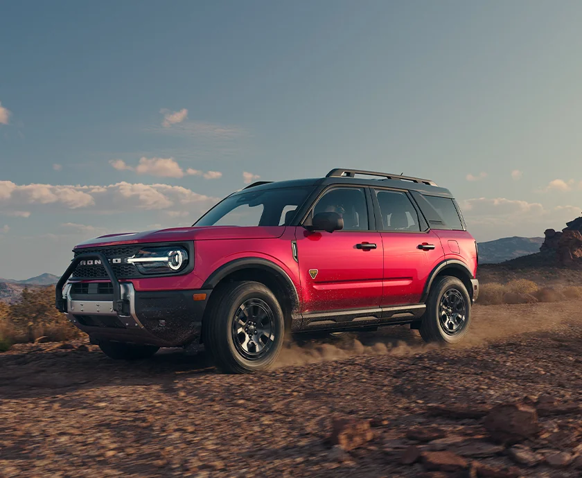 Front side view of a red 2026 Ford Bronco Sport driving though some dirt