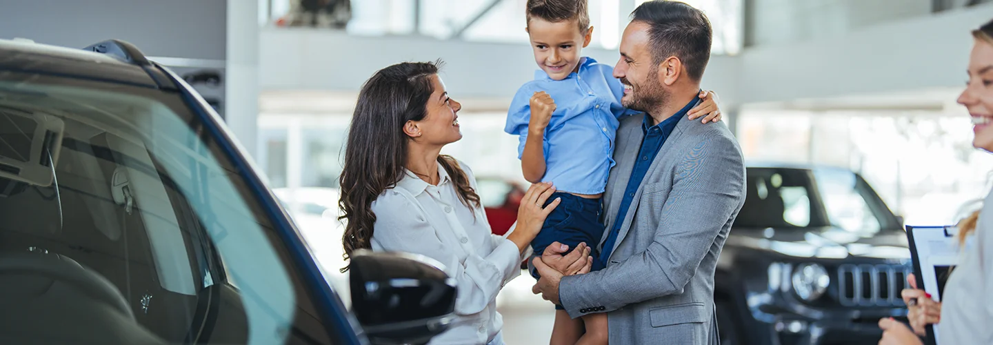 couple holind a child smiling from their purchase of a new car