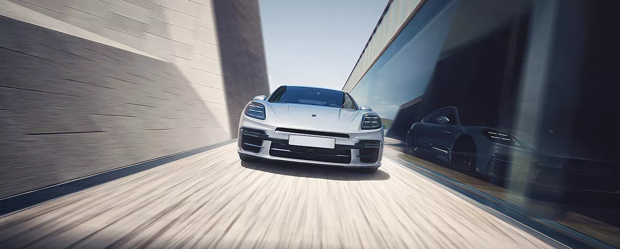 How Far Can a Porsche Hybrid Drive on Electric Power Alone? in Luxury performance sedan driving at high speed on a modern roadway with motion blur and reflective glass surroundings