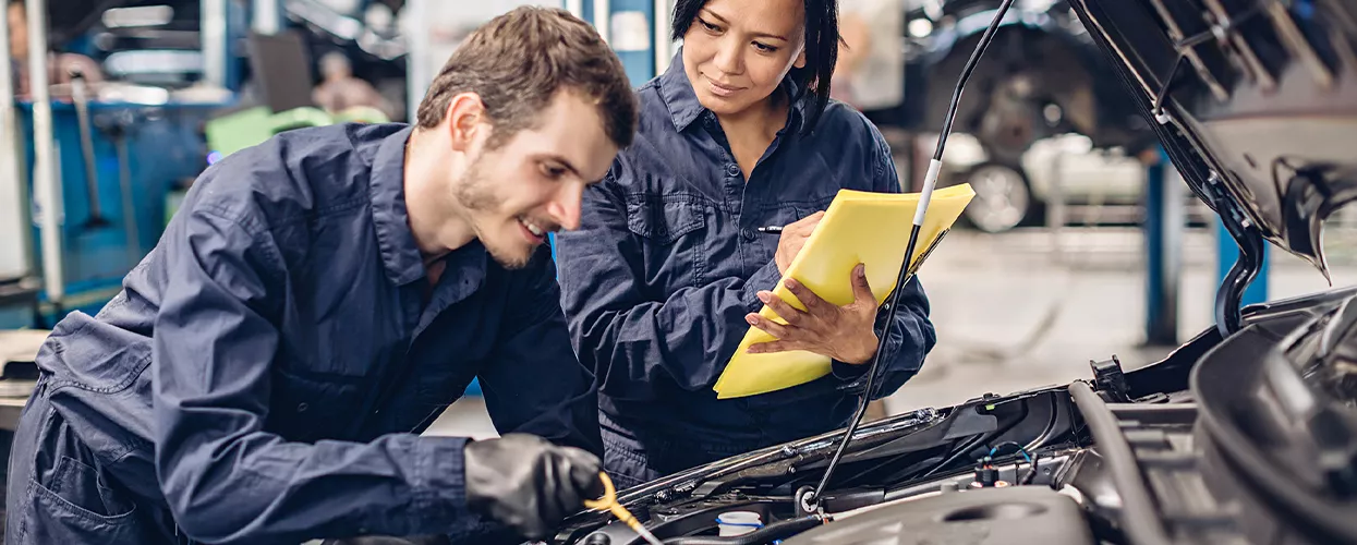 Two service mechanics working under the hood of a vehicle