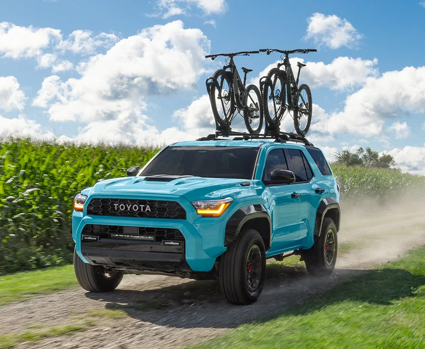 Front view of a blue 2026 Toyota 4Runner driving on a dirt road with 2 bikes on the its roof