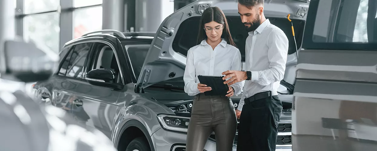 Car salesman and saleswoman looking at a tablet in a car dealership