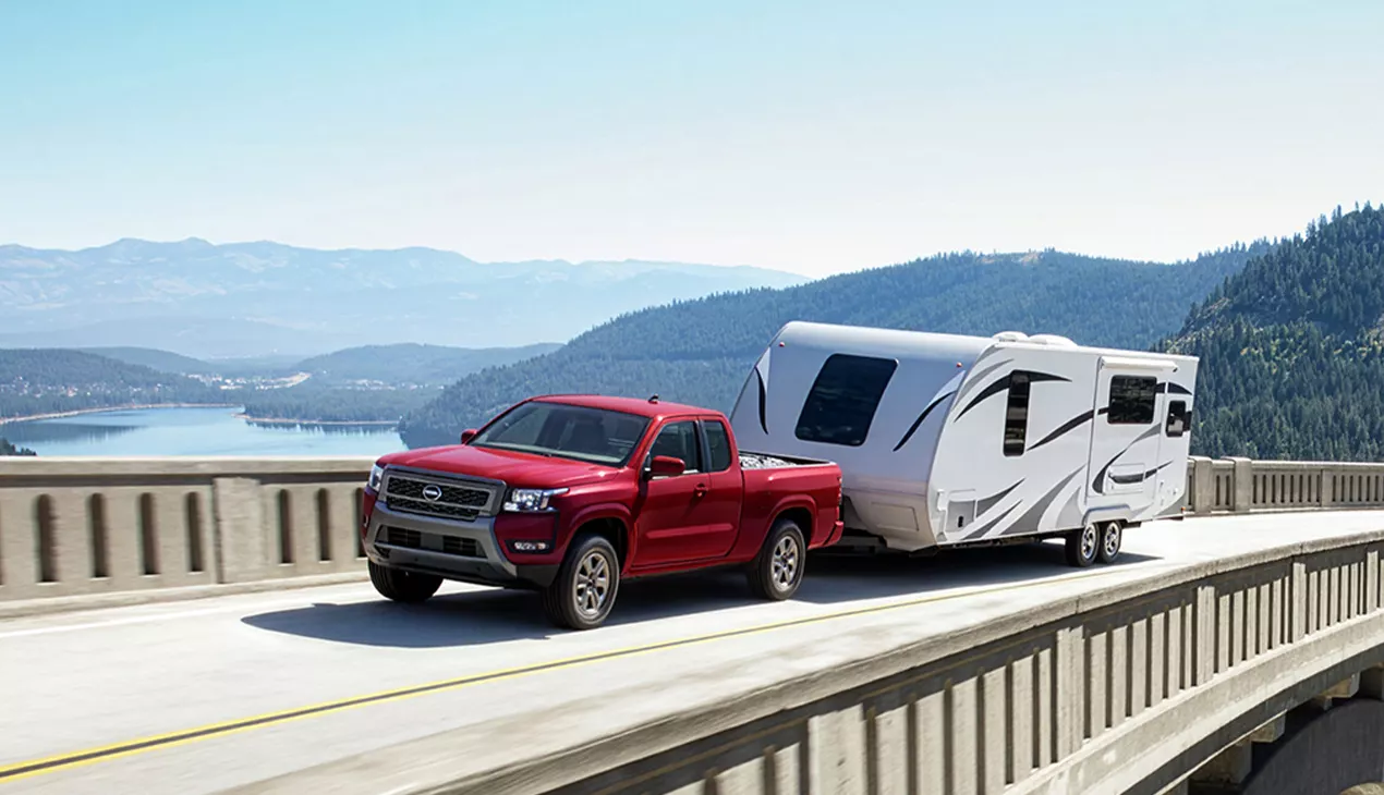 Red Nissan truck pulling a camper over a bridge