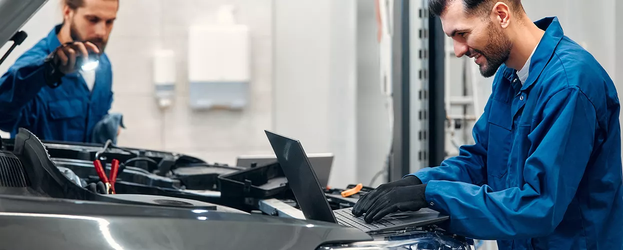 Certified automotive technicians performing vehicle diagnostics and maintenance using advanced computer diagnostic tools