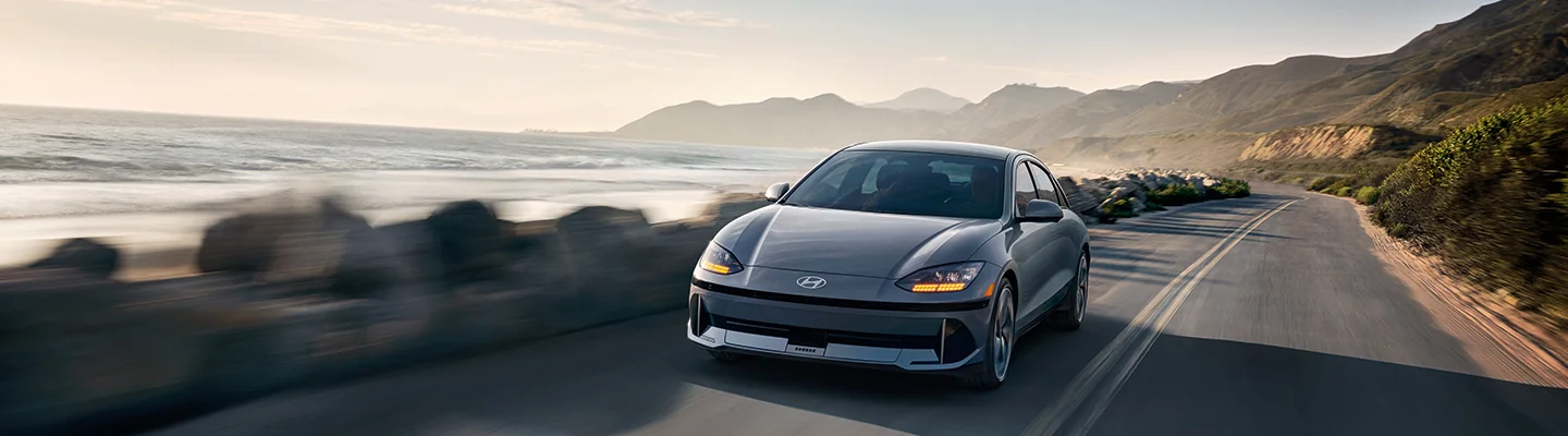 A gray Electric Hyundai Model driving down a sea side road