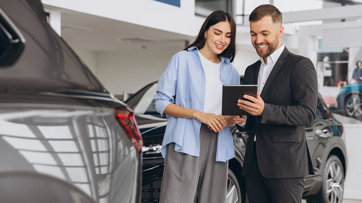 car salesperson showing another person specification on a new car purchase in the deaership showroom