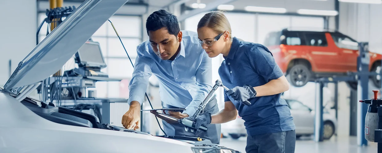 Two auto mechanics collaborating on car maintenance in a garage, with tools and parts visible around them.