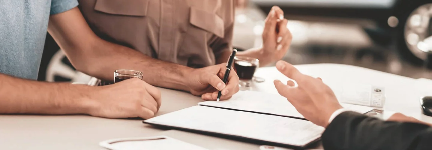 two people on one side of desk showing hands, one signing and on other side of table hands of the salesperson