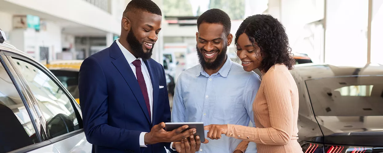 A car salesman showing a couple a tablet in a car dealership