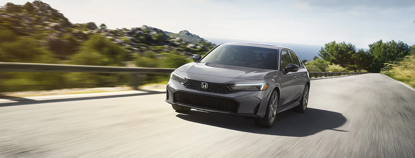 Front view of a 2025 Honda Civic Sport driving on a scenic road