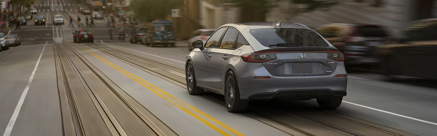 Back view of a gray 2025 Honda Civic Sport driving down a city street