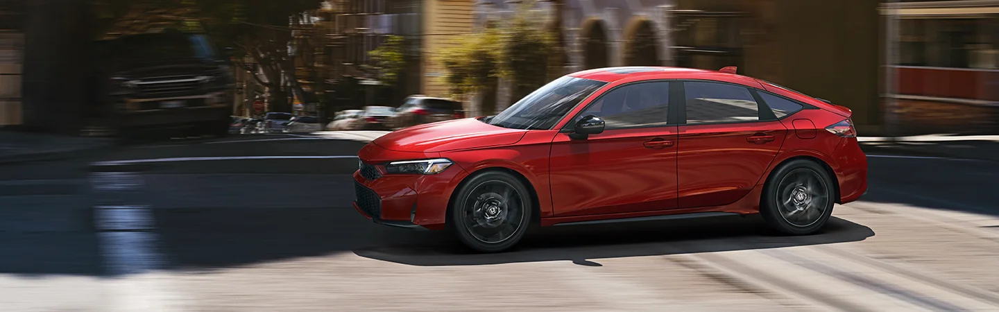 Side view of a red 2025 Honda Civic Sport driving in the city