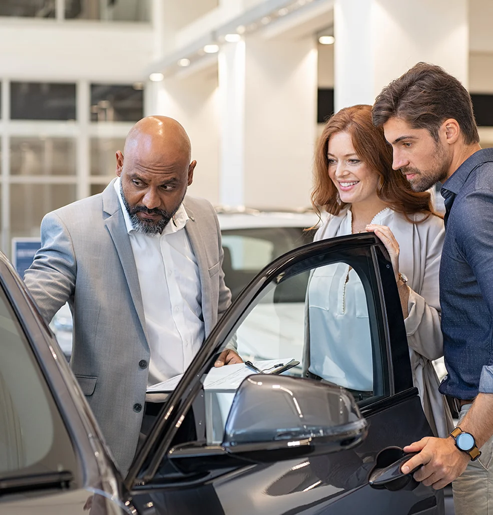 A man and woman standing beside a car, engaged in conversation about its design and performance.