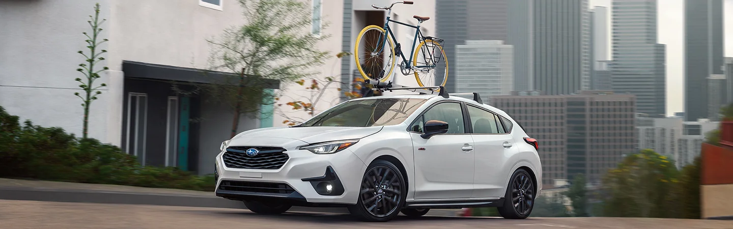 A white 2025 Subaru Impreza driving in the city with a bike on a bike rack on it in Leesburg, FL.