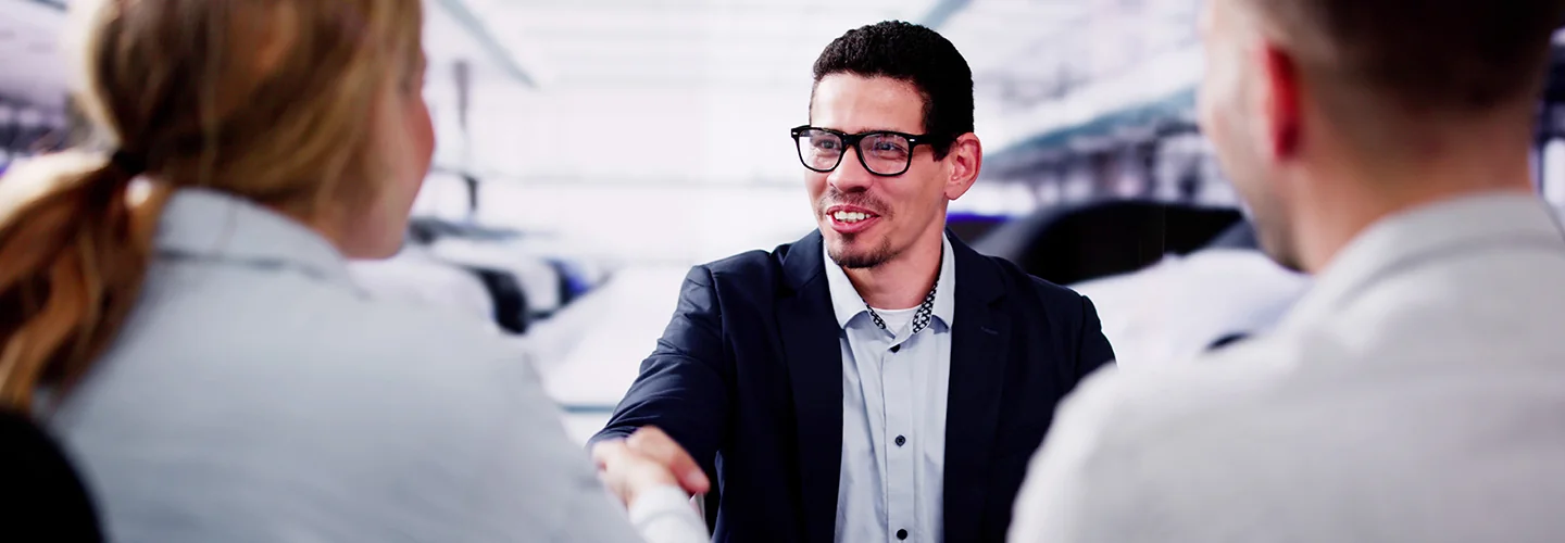 Customers sit with a car salesperson in a dealership