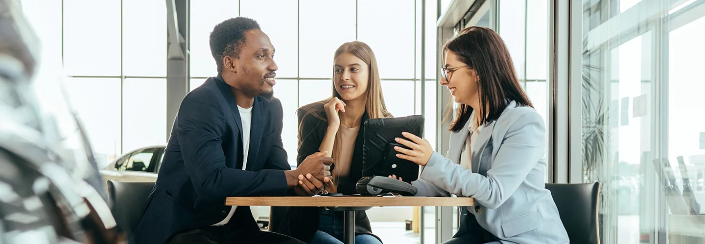 Three people sitting around a table lookig at a tablet and talking