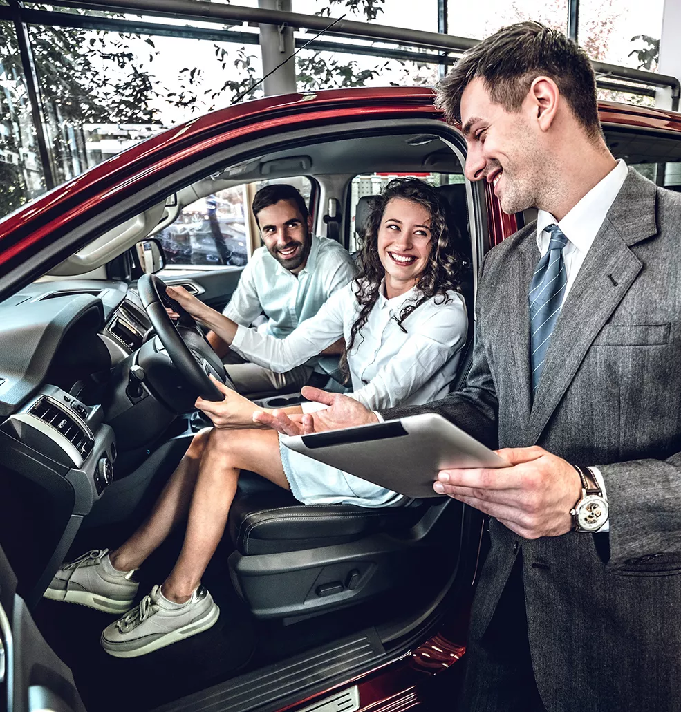 Couple sitting in a new car with a car salesman talking to them