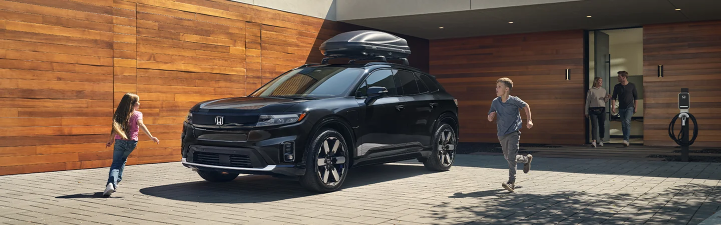 2025 Honda Prologue EX parked in front of home with luggage carrier strapped to top, kids running around car with grownups coming out of house