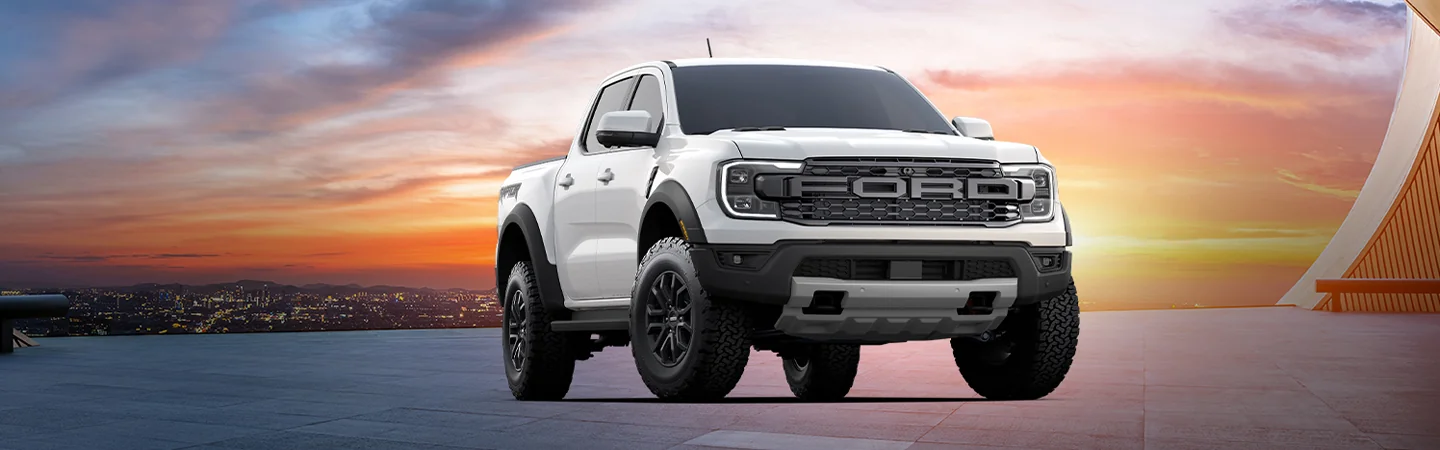 A parked white 2025 Ford Ranger Raptor with a city in the background