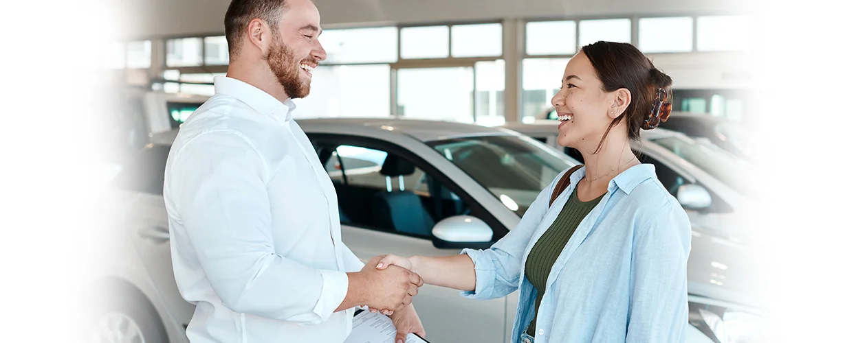 A man and woman are shaking hands in front of a car, indicating a successful negotiation or collaboration.