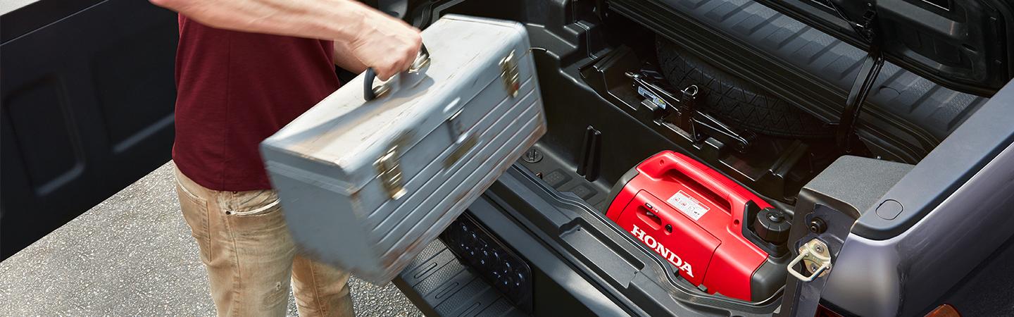 A guy loading tools into a 2021 lockable In-Bed Ridgeline trunk