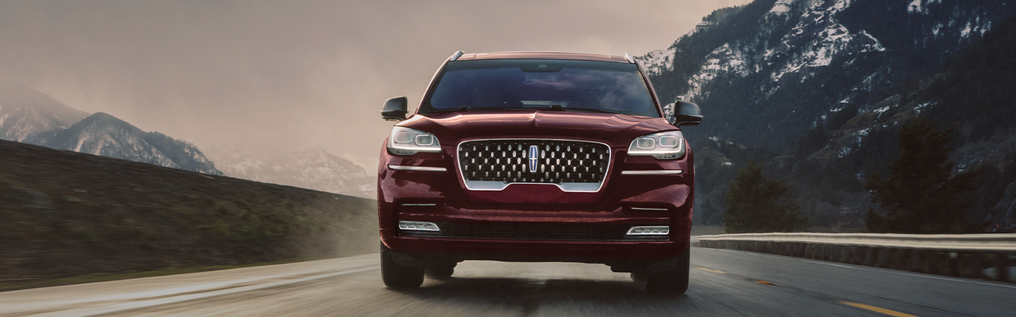 Front view of a red Lincoln Aviator driving through the mountains