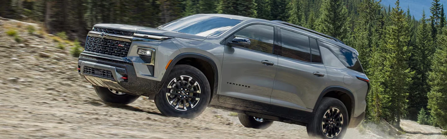 Side view of a parked 2024 Chevrolet Traverse on dirt by a forest